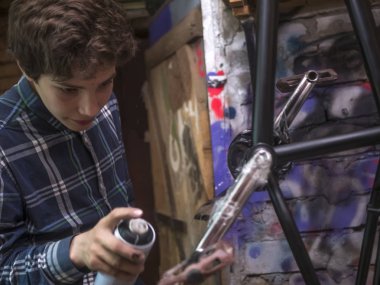 Genç adam sprey ile bmx bisiklet boyama yakından atölyesinde olabilir