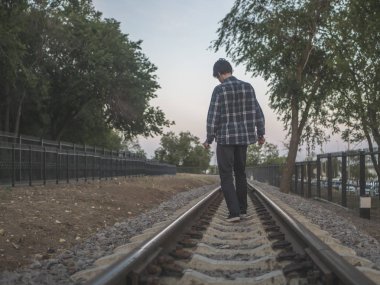 ağaçlar arasında tren yolu üzerinde yürüyen genç yalnız adam