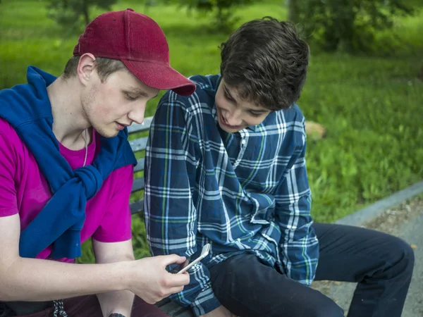 Två Leende Handsome Bröder Kontrollera Foto Mobiltelefonen Sitter Bänken — Stockfoto