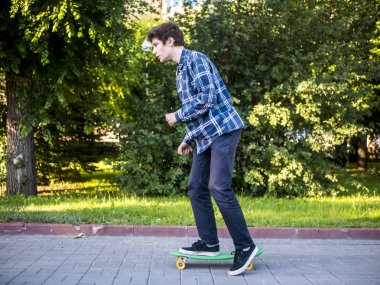 Genç adam rahat kıyafetler şehir parkında kaykay hızlı hızlı sürme yan görünüm