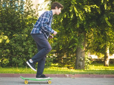 Genç adam rahat kıyafetler şehir parkında kaykay hızlı hızlı sürme yan görünüm