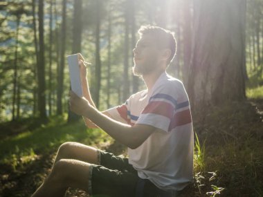 güneşli bir günde orman ve not defterinde yazılı şiir rahat oturan genç handscome adam zemin