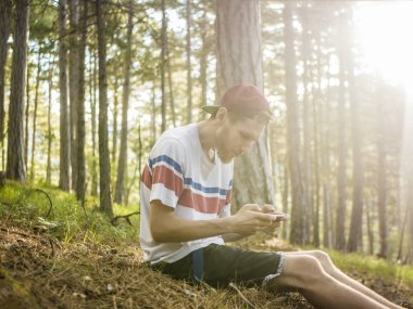hipster kap ve milli park ormanda oturan ve sosyal ağ telefonu sohbet rahat kıyafetler oung sakallı