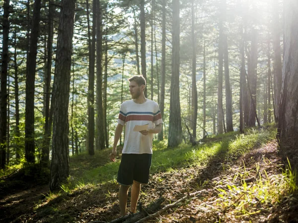 Genç adam şair sketchbook güneş ışığı ve yazma şiir altında ormanda yürüyüş