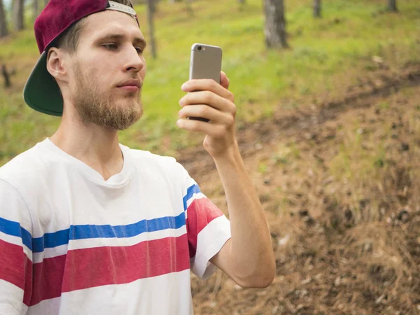 스위스 소나무 숲에서 전화를 사진을 수염된 젊은이 닫습니다 — 스톡 사진