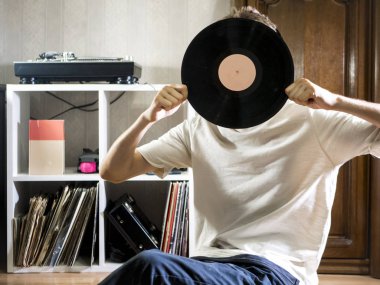 Vinil kaydı diskini kayıtları raf yakınındaki yerde tutarak rahat oturma odasında oturan genç adam