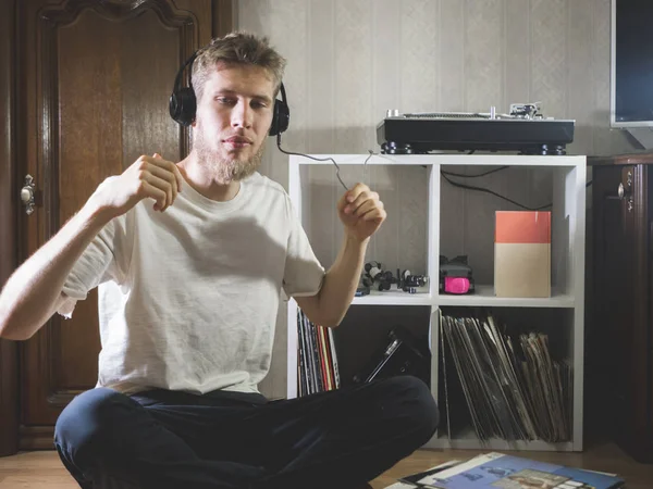 vintage young bearded man listen music with headphones sitting on the floor at home near record player