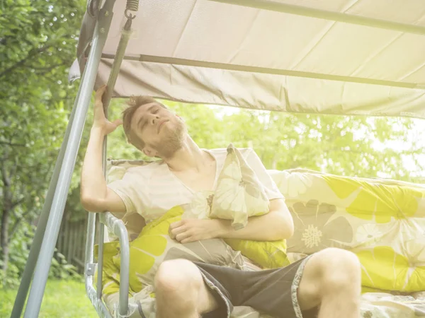 Nuori Parrakas Mies Istuu Rentouttava Puutarhassa Keinu Sohva Kesäpäivänä — kuvapankkivalokuva
