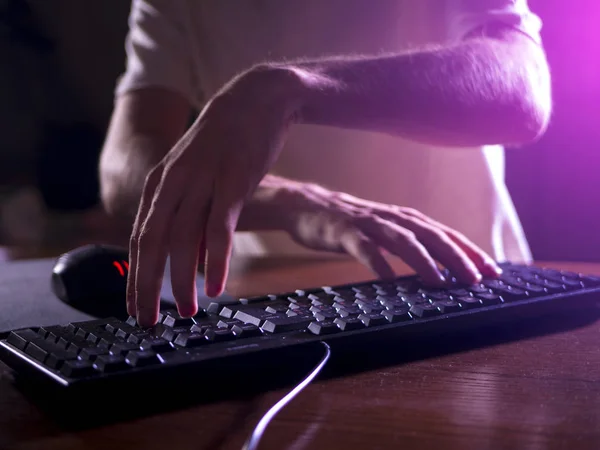 close up gamer hands on the keyboard playing video games in the night