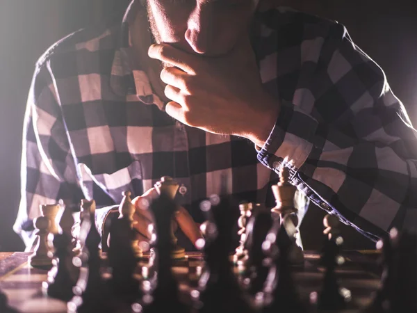 young unrecognizable male person thinking near the chess board concept with dark background