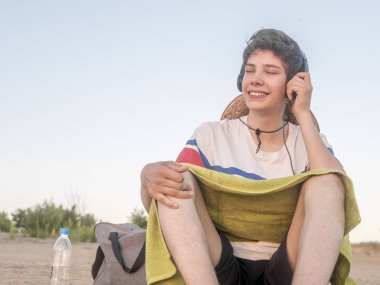 Genç hipster sahil kumu yaz gününde ürpertici kulaklık ile müzik dinlemek