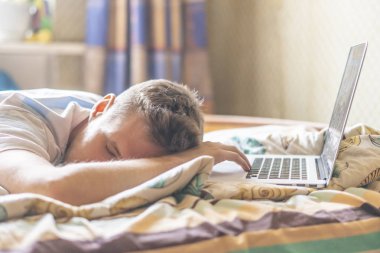 yalan ve gece f içinde laptop üzerinde çalıştıktan sonra güneşli sabah yatakta uyuyan genç kişi