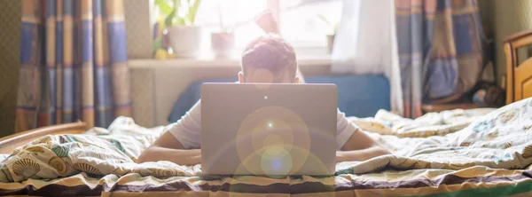 Człowiek w praca dorywcza na laptopa leżąc w łóżku w domu f — Zdjęcie stockowe