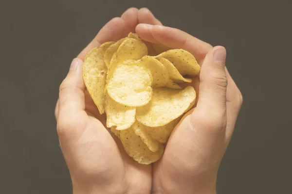 Sopra la testa delle mani tazza tenendo patatine salate su sfondo scuro f — Foto Stock