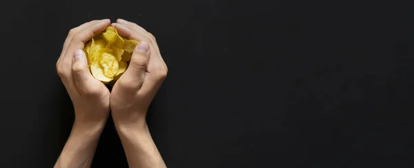 Mani tazza tenendo malsano cibo spazzatura patatine croccanti con spazio copia su sfondo scuro d — Foto Stock