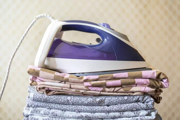 A stack of textile bed sheets blankets with iron on top  f — Stock Photo, Image