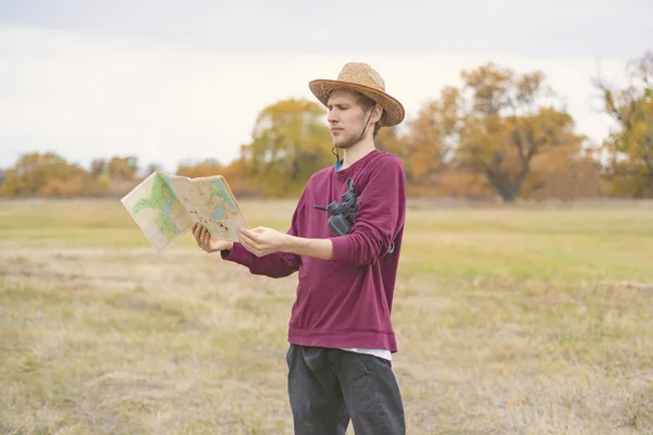 young bearded man in summer hat lost in the forest and search the road on map  f