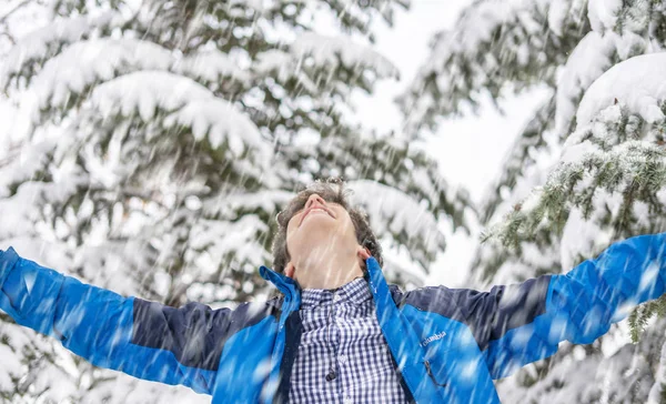 Happy teenage guy enjoying snowfall in the winter snowy forest f — Stock Photo, Image
