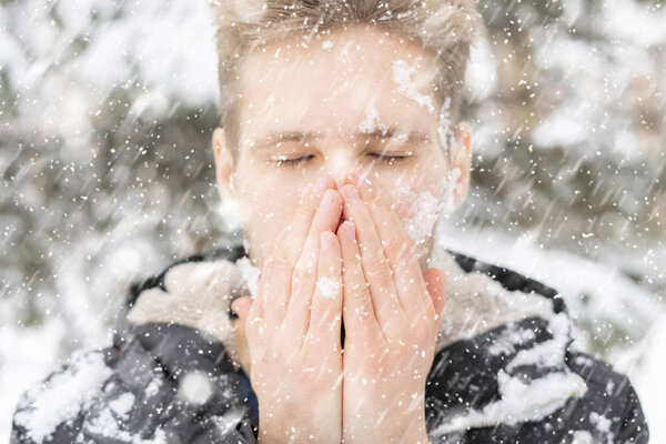 close up man portrait warm up and heating hands near mouth outdoors on a winter day