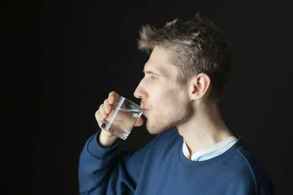 Schöner junger durstiger Mann trinkt gefiltertes Wasser aus Glas — Stockfoto