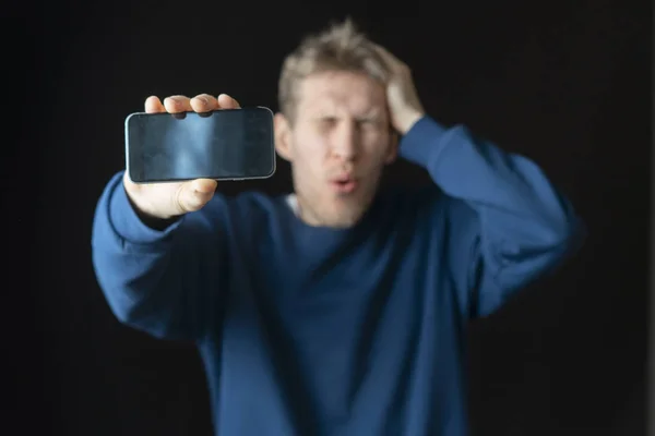 Nuori mies ottaa selfien itsestään matkapuhelimellaan tummalla taustalla b — kuvapankkivalokuva