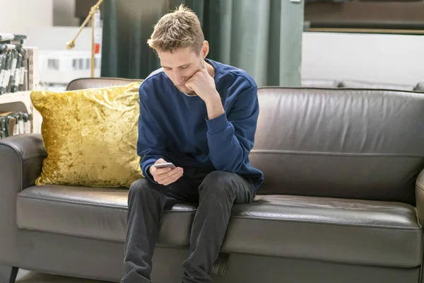 Nuori parrakas mies käyttää älypuhelinta istuu sohvalla f — kuvapankkivalokuva