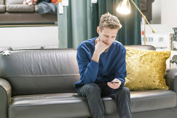 молодой бородатый мужчина с помощью смартфона, сидящий на диване
