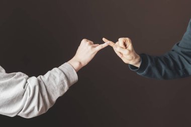 İki adam serçe parmaklarını tutarak barış yapıyor.