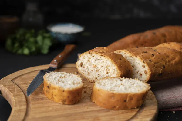 Rozřezané francouzské bagety na dřevěné desce, chléb s chlebem, tmavé pozadí — Stock fotografie