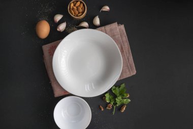 siyah masa üzerinde boş beyaz seramik plaka, yemek pişirmek için taze malzemeler, karabiber, sofra