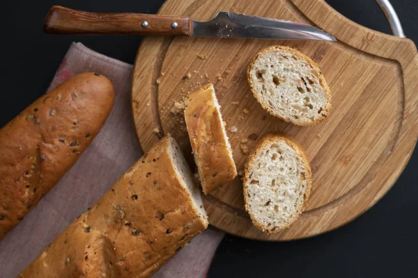 Rozřezané francouzské bagety na dřevěné desce, chléb s chlebem, tmavé pozadí — Stock fotografie