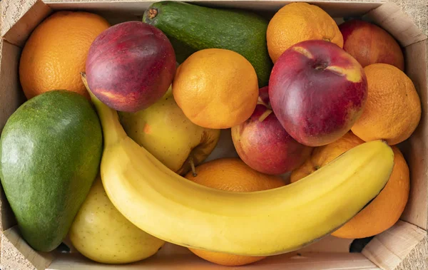 Gran caja de madera con frutas frescas maduras, plátano, manzana, naranja, mandarina, aguacate, alimentos vegetarianos —  Fotos de Stock