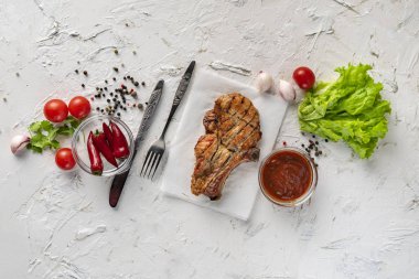 Pişmiş et düzeni, baharat, marul yaprakları, domates, biber ve sos etrafa saçılmış, sofra takımı, bıçak, çatal