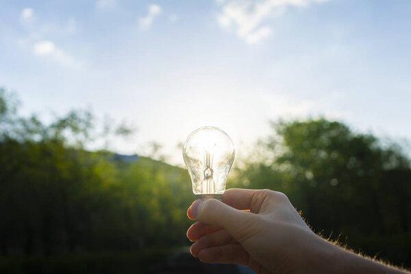 first person view of person hold light bulb outside at the nature, enegry concept with a sunshine through its