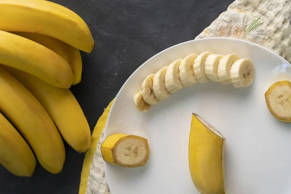 Fresh sliced banana in a white ceramic plate on the black table, preparing ingredients for healthy breakfasts — Stock Photo, Image