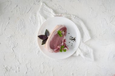 Çiğ domuz eti dilimi ya da beyaz seramik tabakta baharat ve bitkilerle yalıtılmış biftek.