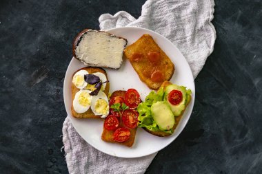 Avokado, yumurta, tereyağı, domates ve reçelli beyaz seramik tabak.
