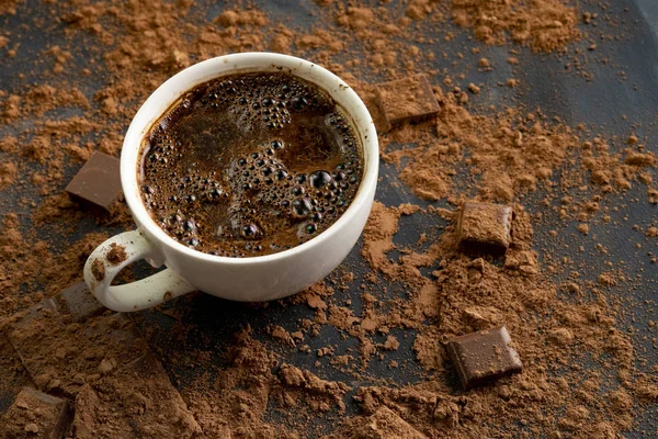 Chocolate caliente fresco al vapor en una taza, barra de chocolate y cacao en las mesas oscuras — Foto de Stock
