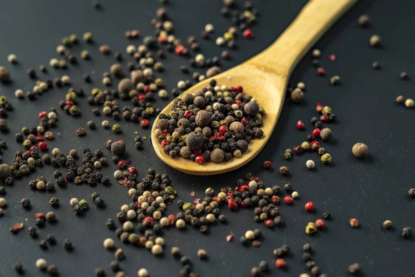 Mischung aus schwarzer Paprika, Holzschüssel oder Kochlöffel, schwarzem Tisch oder Oberfläche — Stockfoto