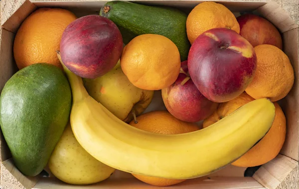 big wooden crate with ripe fresh fruits, banana, apple, orange, mandarine, avocado, vegeterian foods