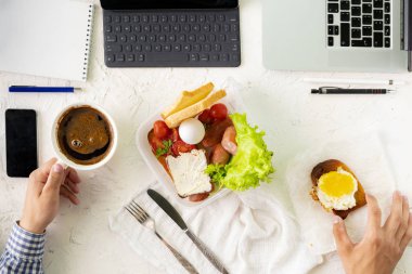 Genç erkek çalışırken laptopun önünde yemek yiyor, kötü alışkanlık ve obezite kavramları