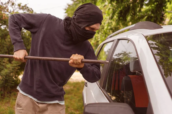 Maskierter Dieb, der in der Nähe des Autos stand und versuchte, mit Kuhstange die Scheibe einzuschlagen — Stockfoto