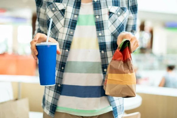 Osoba držící rychlý potravinový balíček a skleničku s obědem v publiki — Stock fotografie