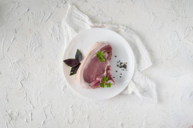 Çiğ domuz eti dilimi ya da beyaz seramik tabakta baharat ve bitkilerle yalıtılmış biftek.