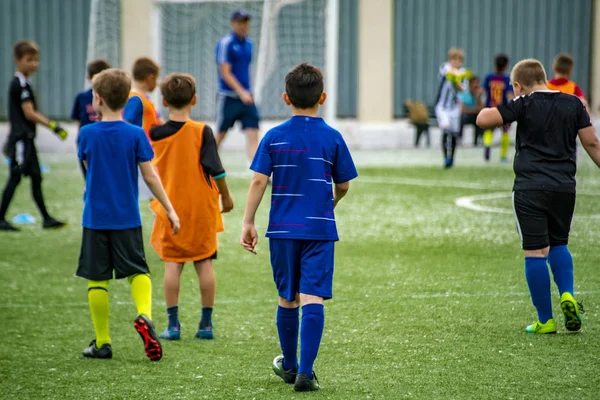 スタジアムの芝生の上でサッカーをしている多くの子供たちを群集する — ストック写真