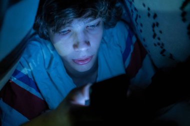 genç çocuk gece battaniye altında yatakta yatan bir akıllı telefon kullanarak