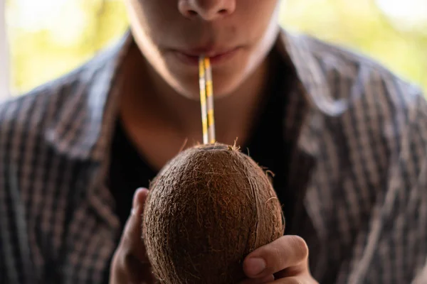 Jovem segurando coco com uma palha e bebendo, close-up — Fotografia de Stock