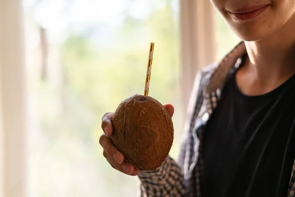 Jovem segurando coco com uma palha e bebendo, close-up — Fotografia de Stock