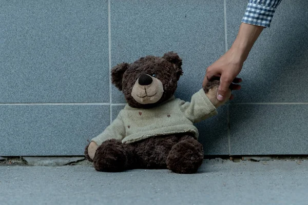 Mão humana agarrar o urso de pelúcia sujo do chão ao ar livre, conceitos perdidos — Fotografia de Stock