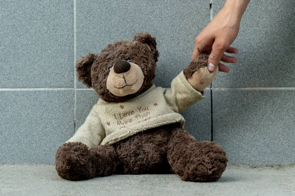 人类的手从室外的地面上抓起肮脏的玩具熊，迷失了概念 — 图库照片